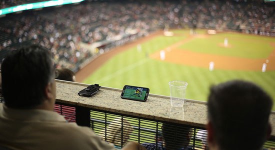 man at baseball game watching football on his phone