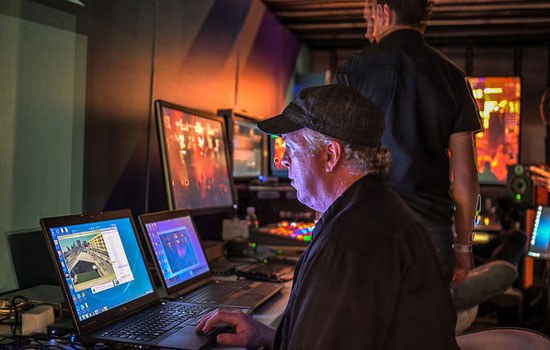 One man sits and another stands in front of several computers and monitors streaming the FADER FORT 2014