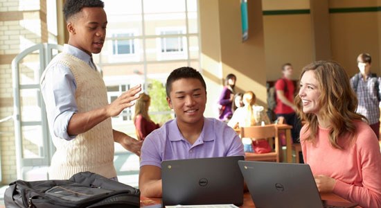 Three students in a cafeteria setting working on Dell laptops