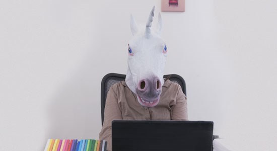 Image of a man with a unicorn head typing on a laptop computer