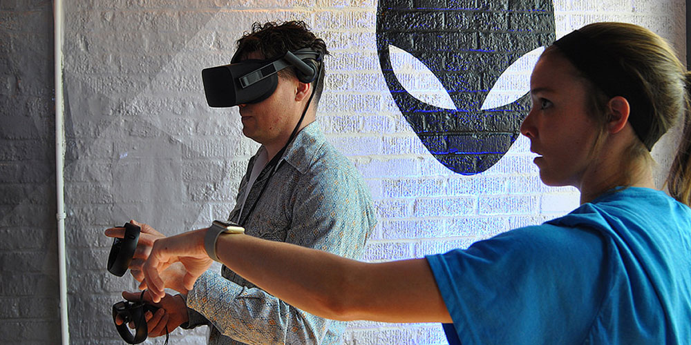 A man plays a virtual reality game in front of the Alienware logo at SXSW 2017