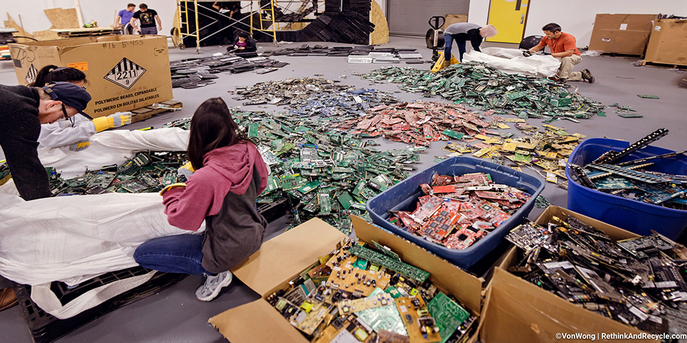 people sitting on the floor of a warehouse sorting through old computer motherboards