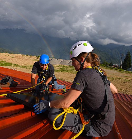 two people installing a solar panel on a roof with a rainbow in the background